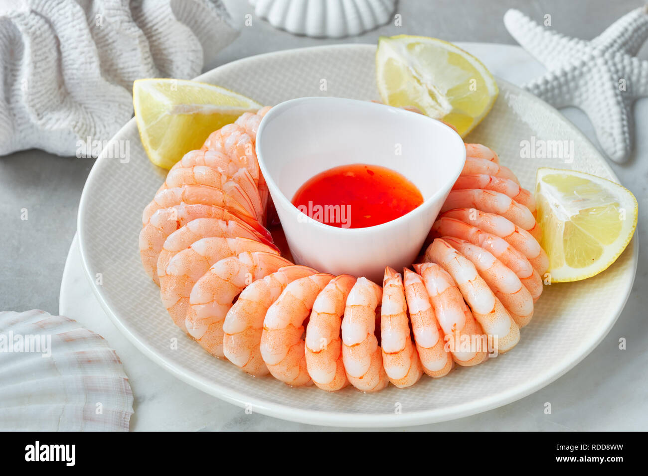 Close-up on shrimp ring with sweet chili sause, dill and  lemon on light background with white sea decorations Stock Photo