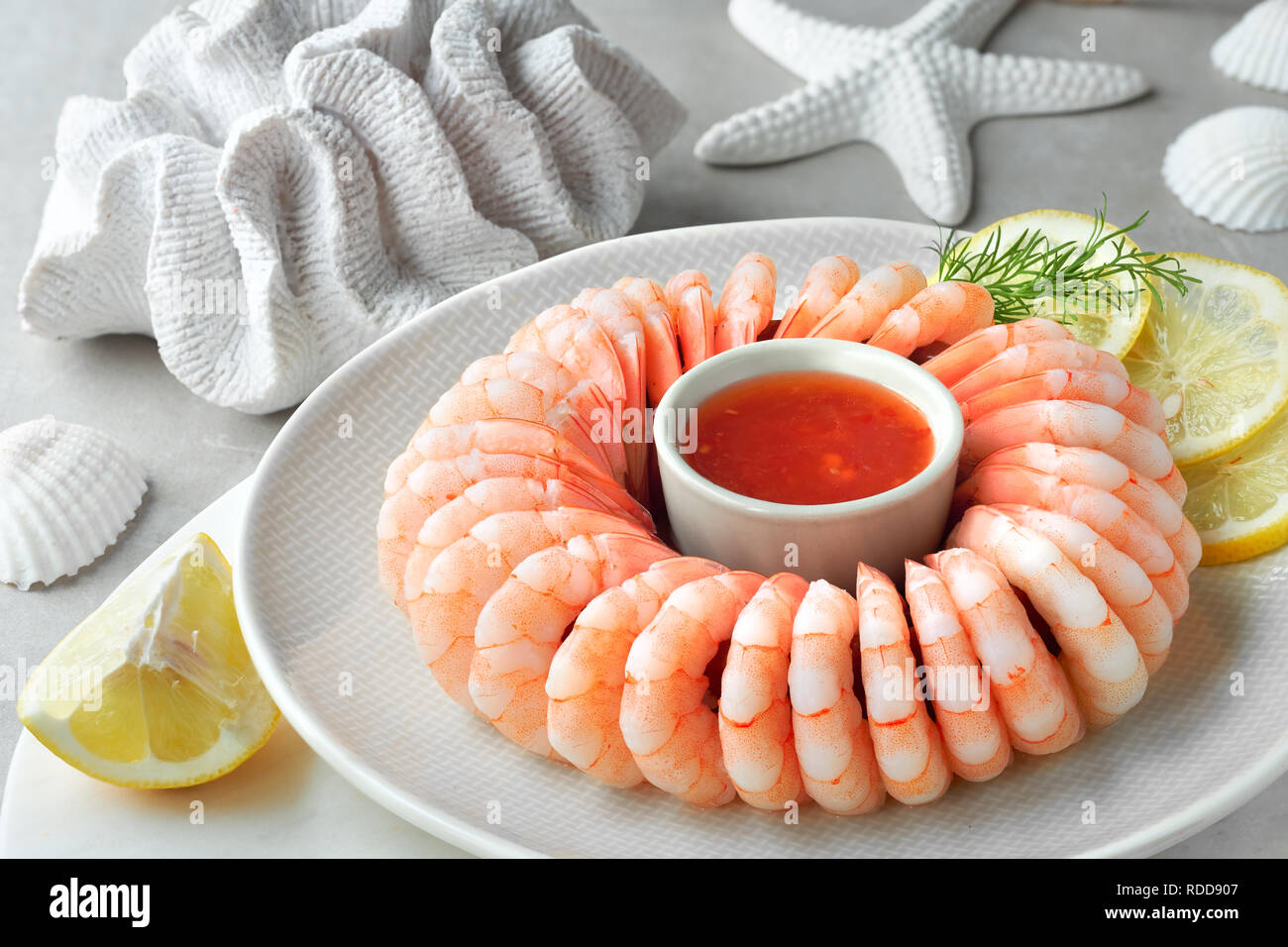 Close-up on shrimp ring with sweet chili sause, dill and  lemon on light background with white sea decorations Stock Photo