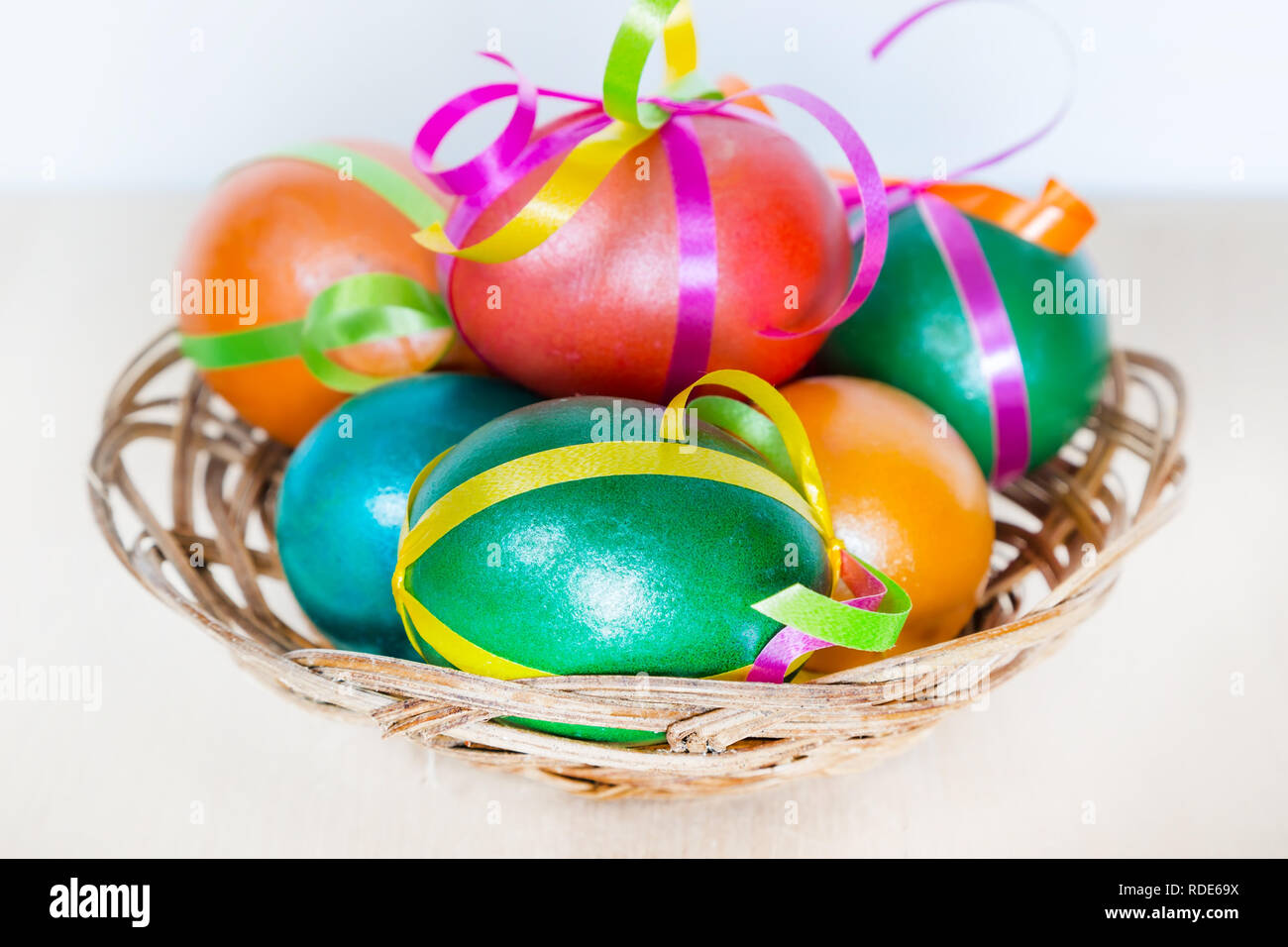 Brightly colored bow decorated easter eggs in basket, holiday background Stock Photo
