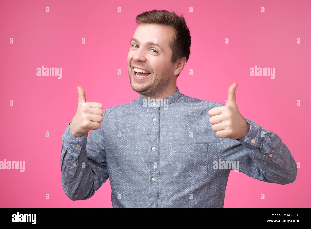 Young attractive man dressed in blue shirt showing thumbs up standing over pink background Stock Photo