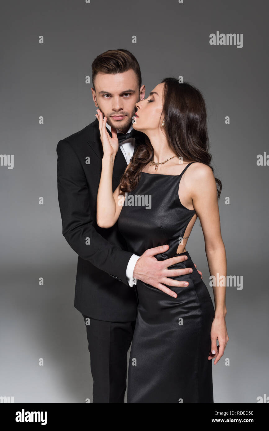 beautiful elegant woman kissing handsome boyfriend isolated on grey ...