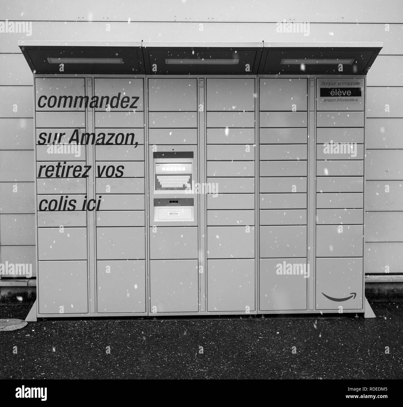 LYON, FRANCE - FEB 4, 2017: Snowing in front of Modern Amazon Locker orange delivery parcel package locker - self-service parcel delivery offered by online retailer Amazon.com - black and white Stock Photo