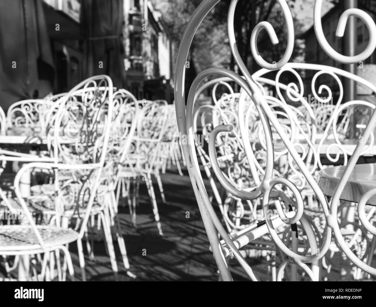 Beautiful forged white metal chairs with pattern in traditional style of an Italian Ice Cream gelateria on the sunny street in German street - black and white . Stock Photo