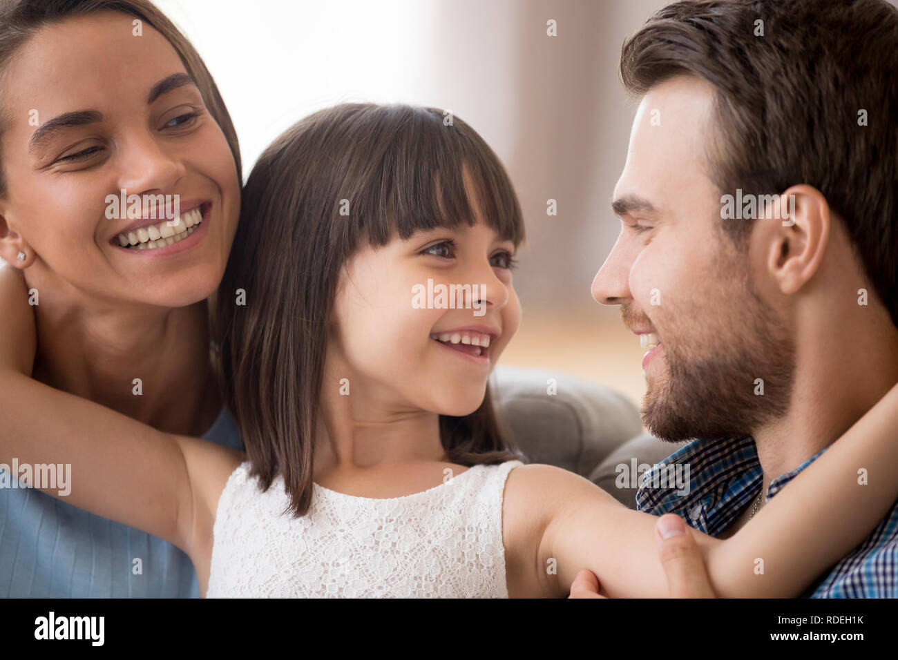 Happy kid daughter embracing parents looking at smiling mom Stock Photo