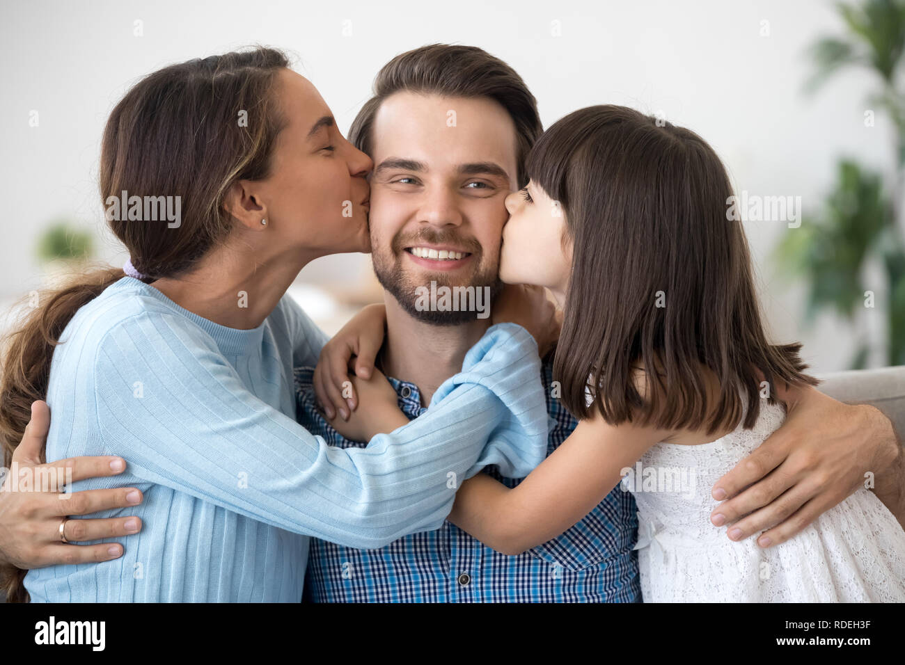 Kid daughter and wife embracing kissing happy father on cheeks Stock Photo