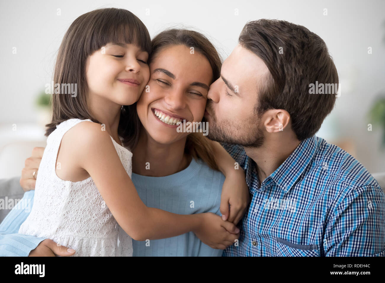 Loving husband and cute kid daughter embracing kissing happy wom Stock Photo