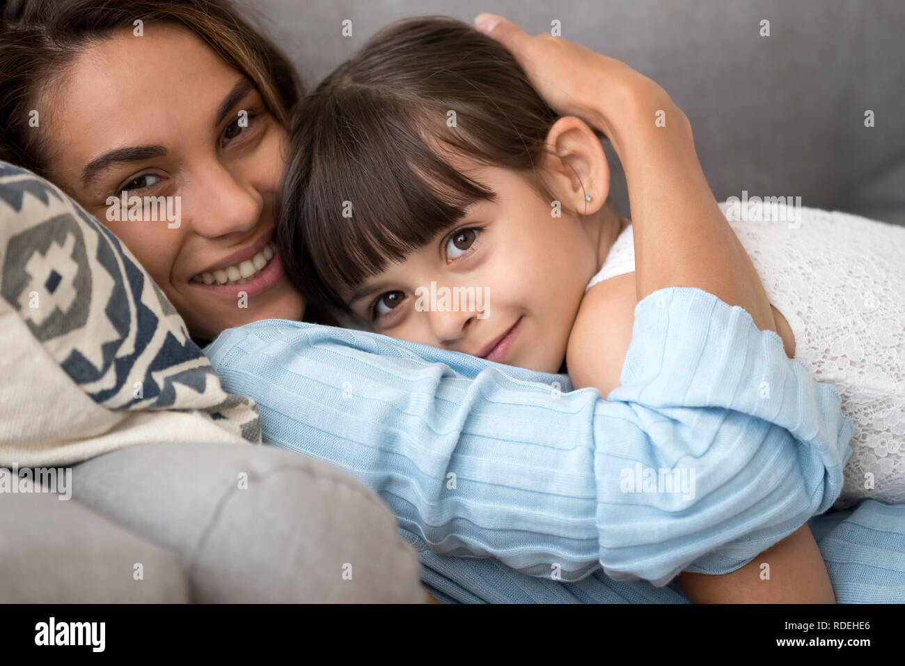 Loving mom embracing adorable kid daughter relaxing on sofa, por Stock Photo