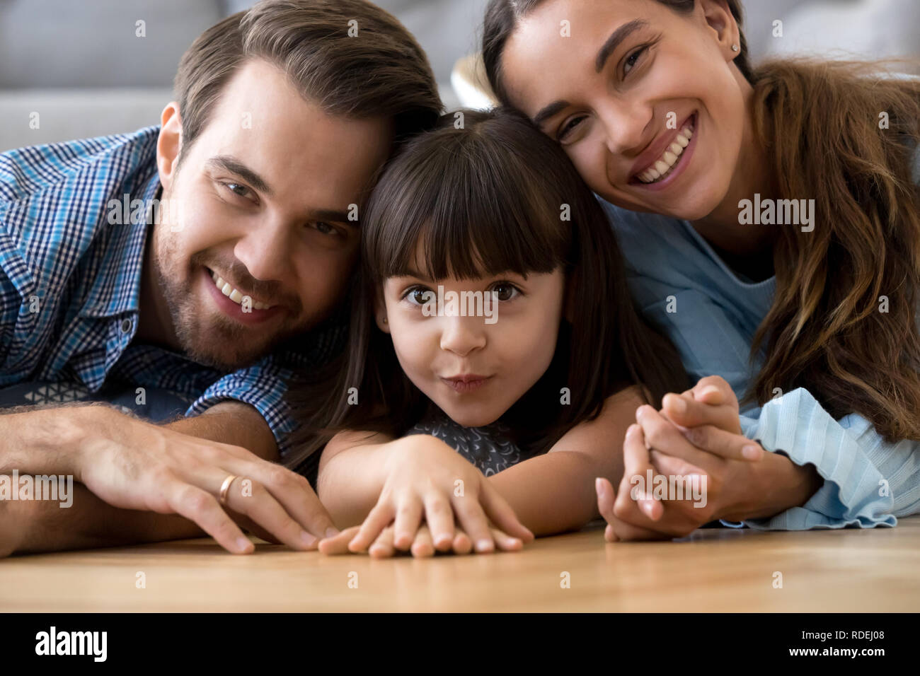 Funny cute little daughter lying on warm floor with parents, por Stock Photo