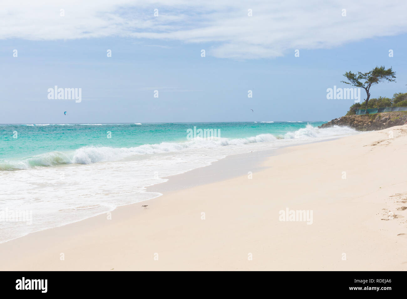 A white beach at Silver Sands on Barbados. Ocean waves roll in. Kitesurfers play in the safe waters off-shore. Stock Photo