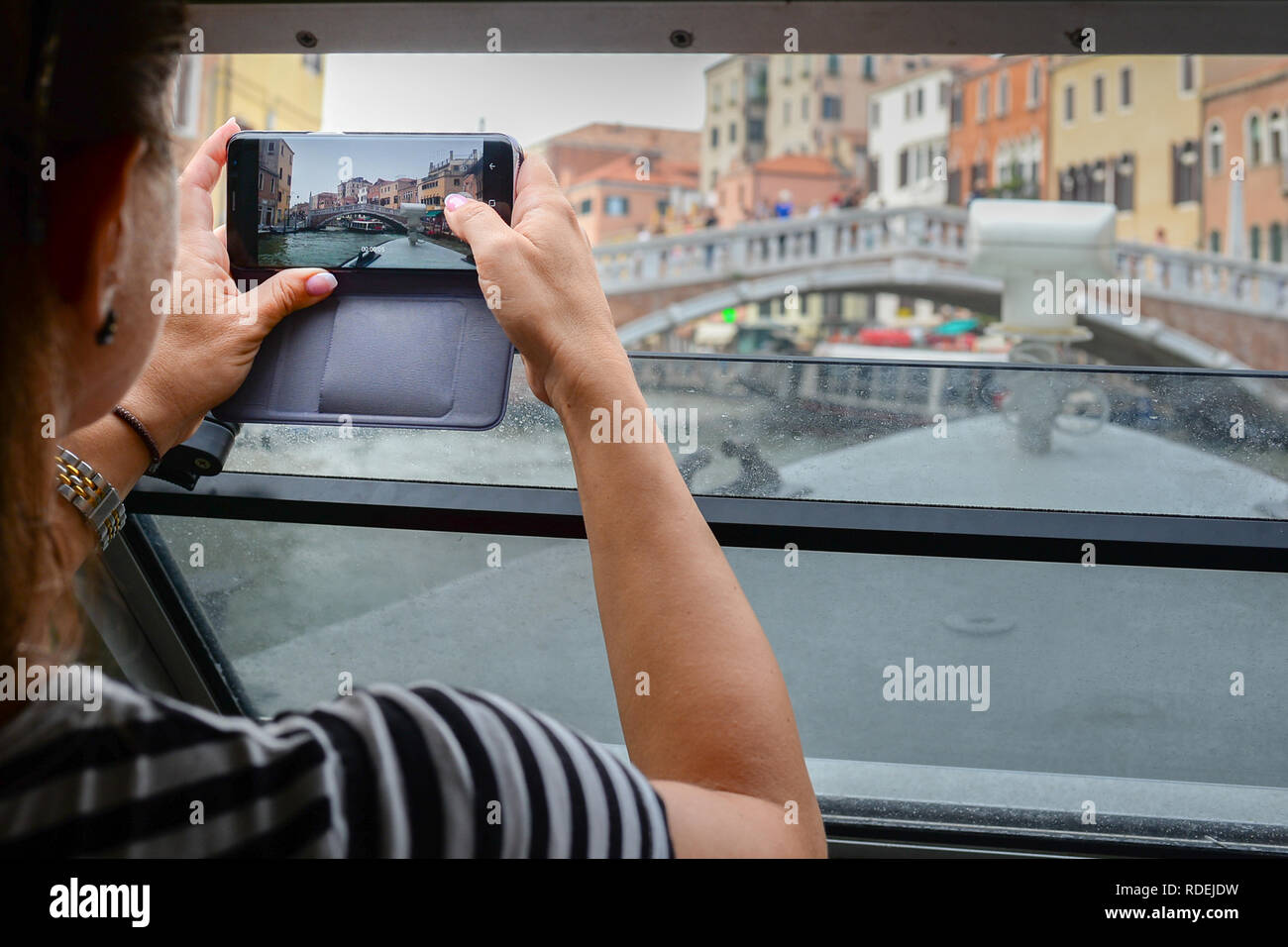 women's hands hold mobile and photograph a bridge in Venice from vaporetto Stock Photo