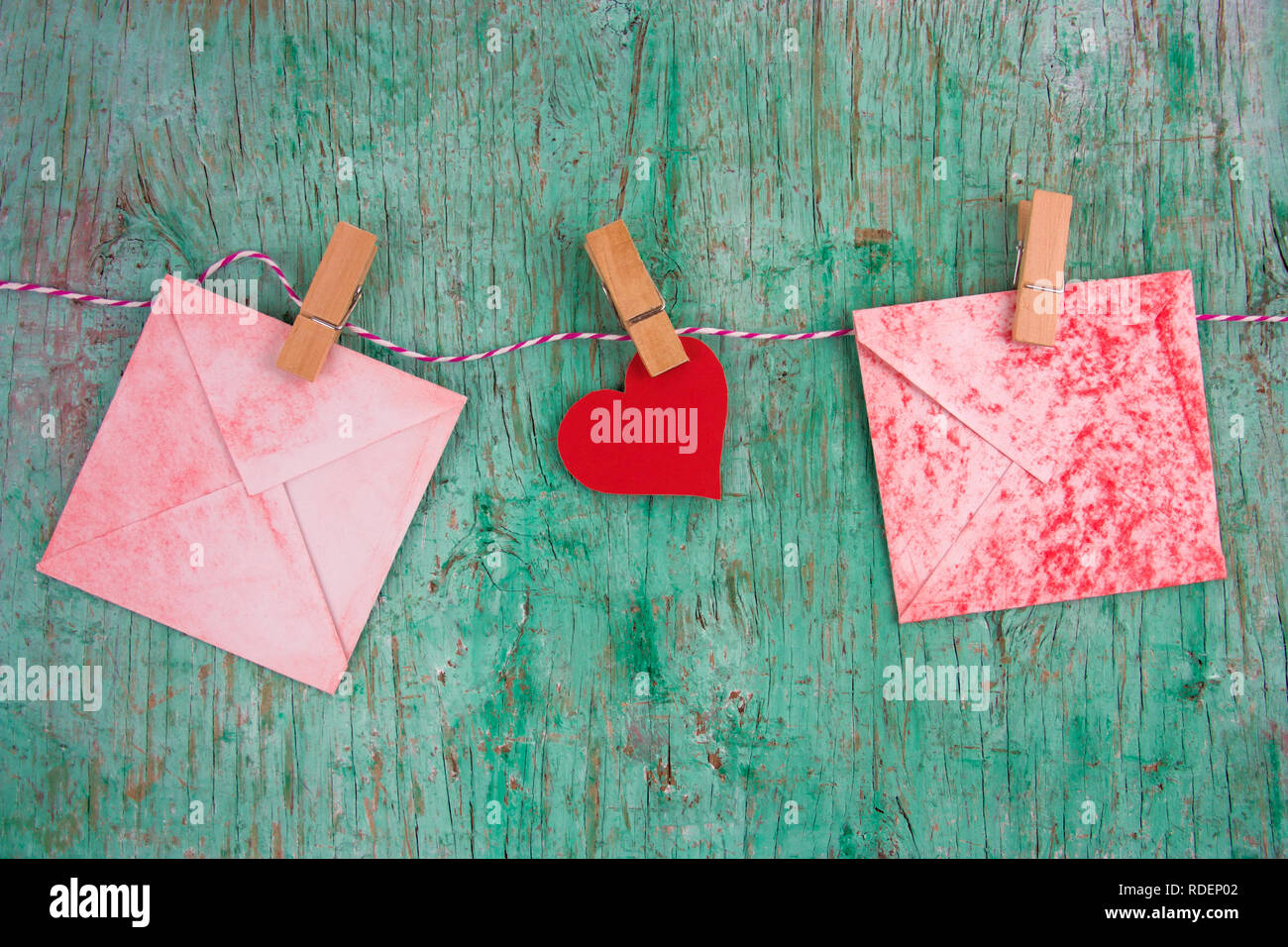 vintage  red paper envelops and paper red heart hung on clothespins on a rope on a mint green wall background Stock Photo