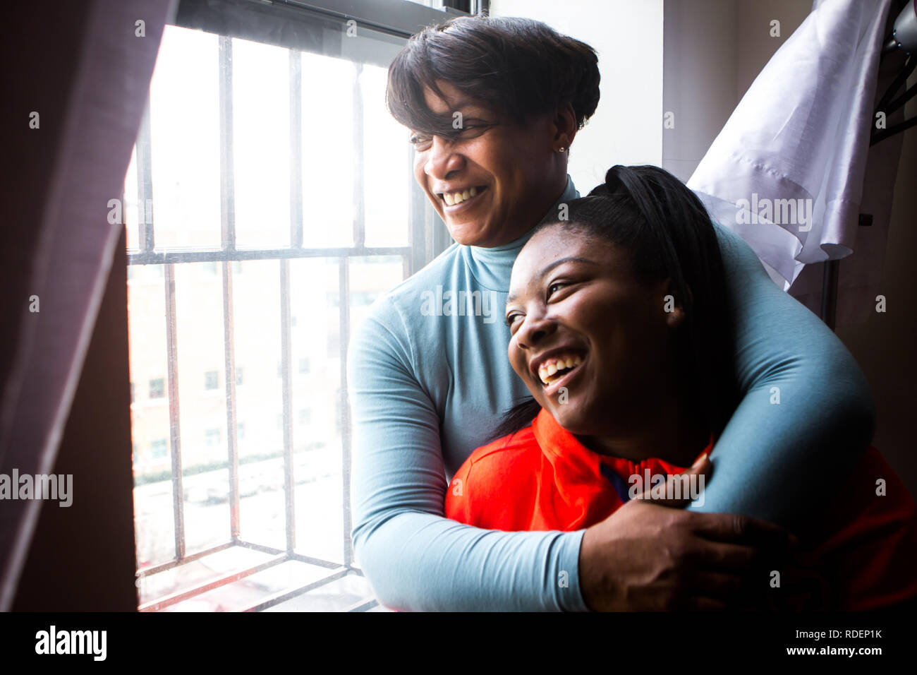 Black mother and teenage daughter laugh looking out window with bars in the city Stock Photo
