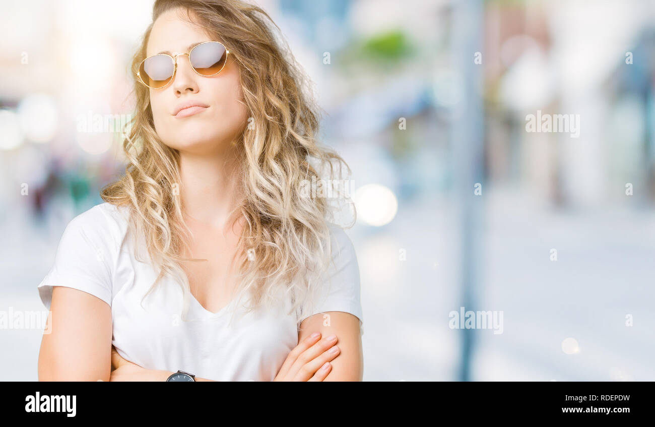 Beautiful young blonde woman wearing sunglasses over isolated background skeptic and nervous, disapproving expression on face with crossed arms. Negat Stock Photo