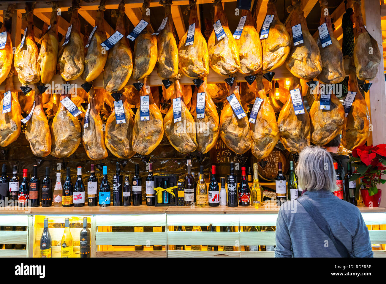 Hanged Jamon and vine bottles on Valencia central market. Drycured ham from Spain. Woman