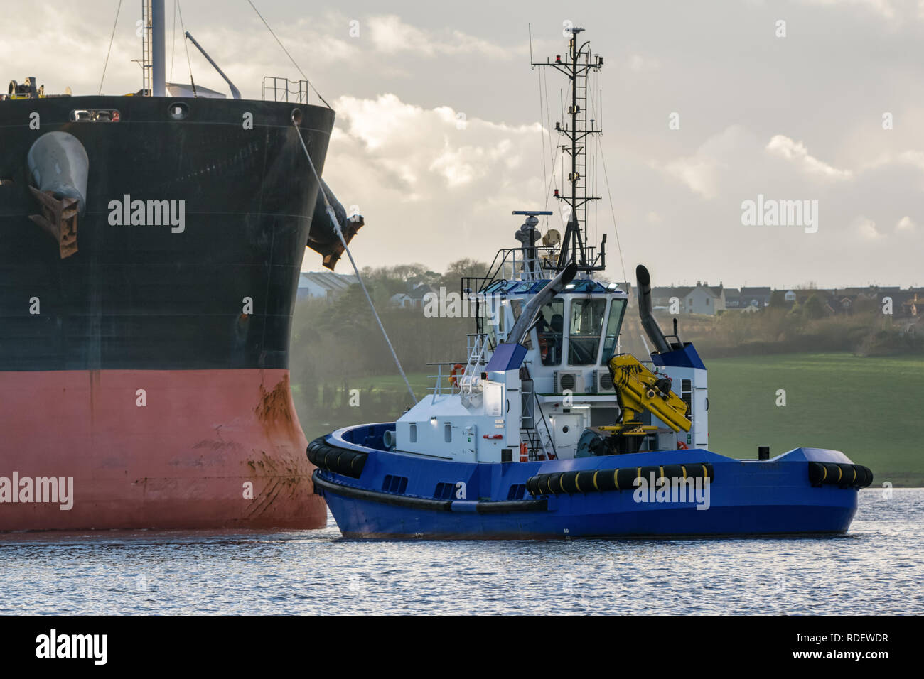 A picture of a cargo ship coming into harbour being towed by a tug boat Stock Photo