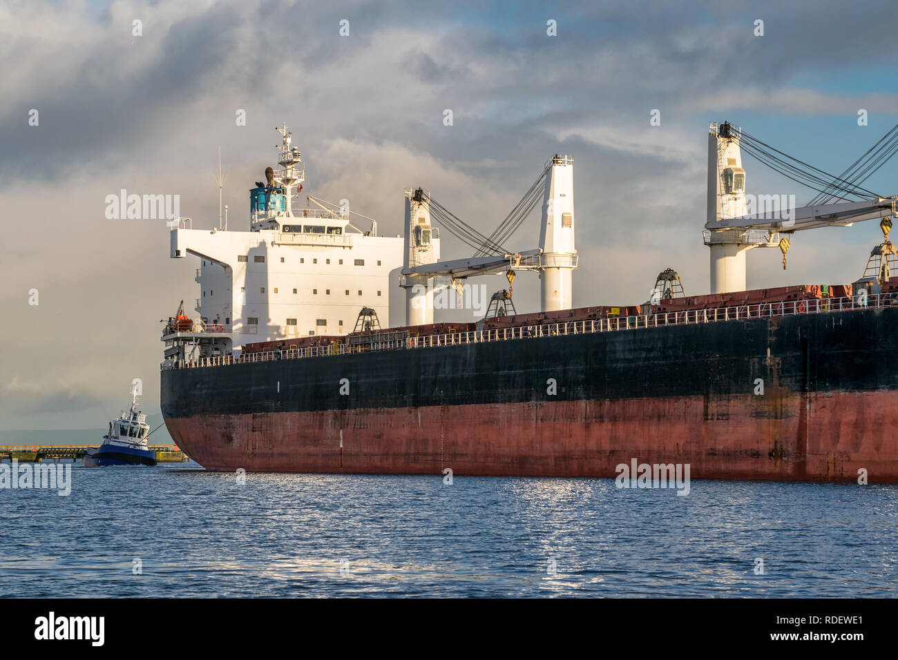 A picture of a cargo ship coming into harbour being towed by a tug boat Stock Photo