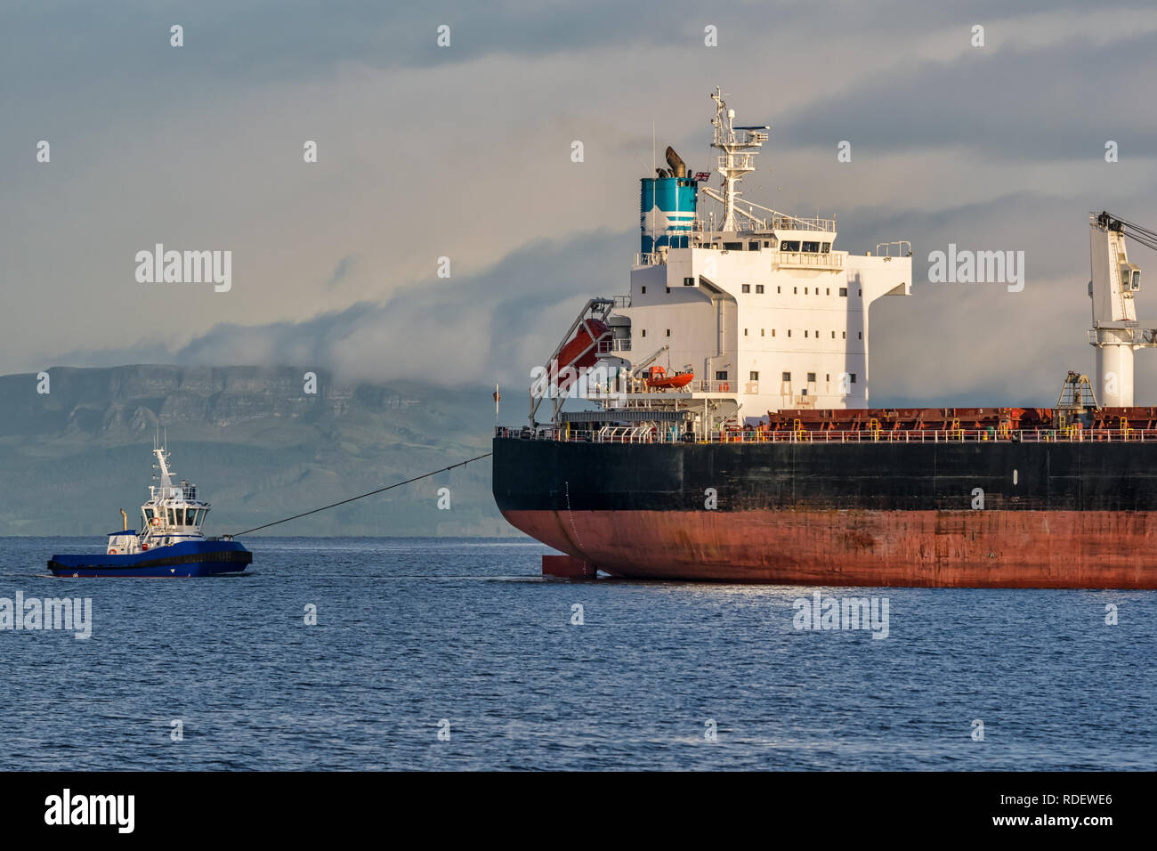 A picture of a cargo ship coming into harbour being towed by a tug boat Stock Photo