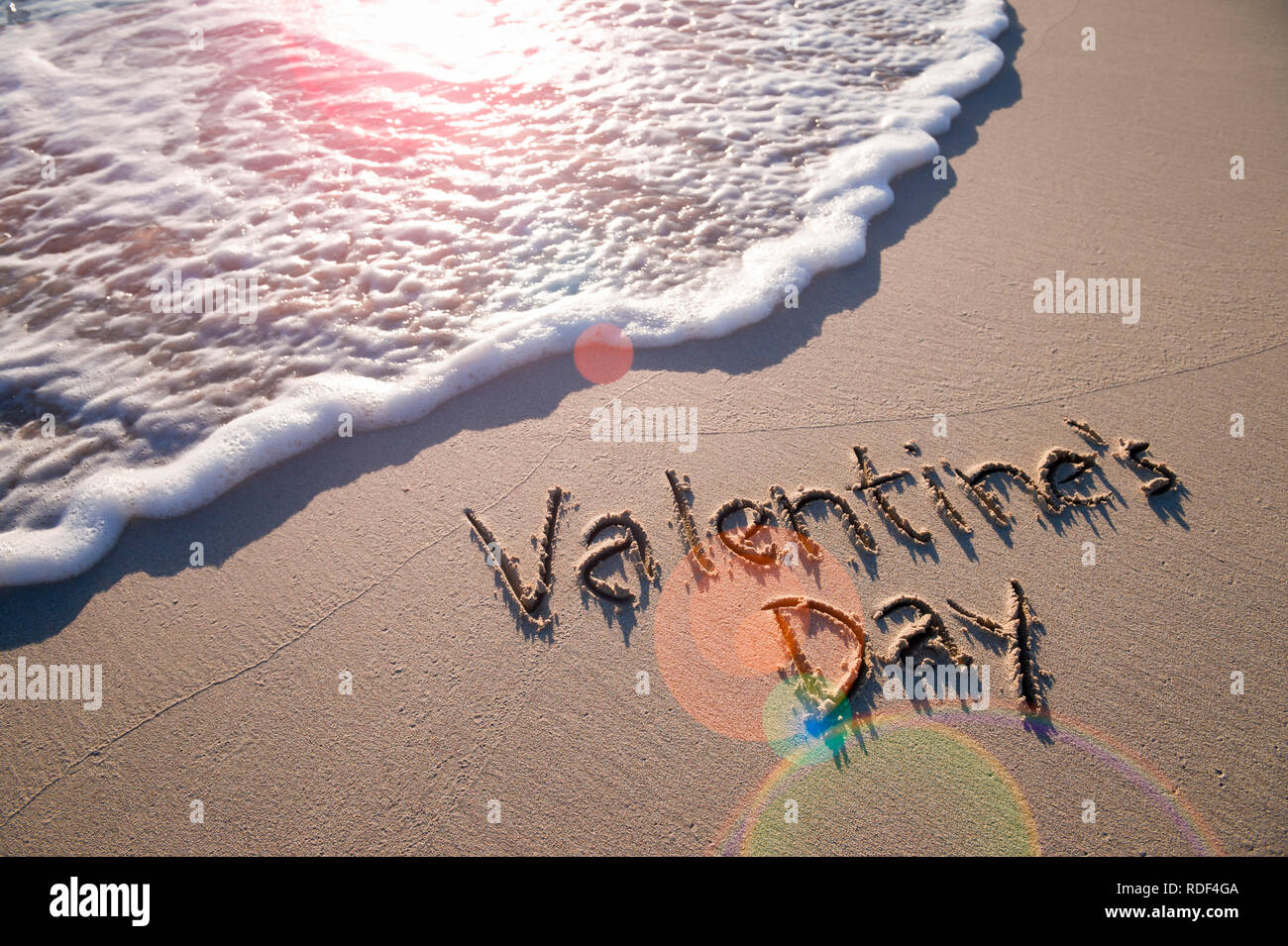 Valentine's Day message handwritten on smooth sand beach with lens ...