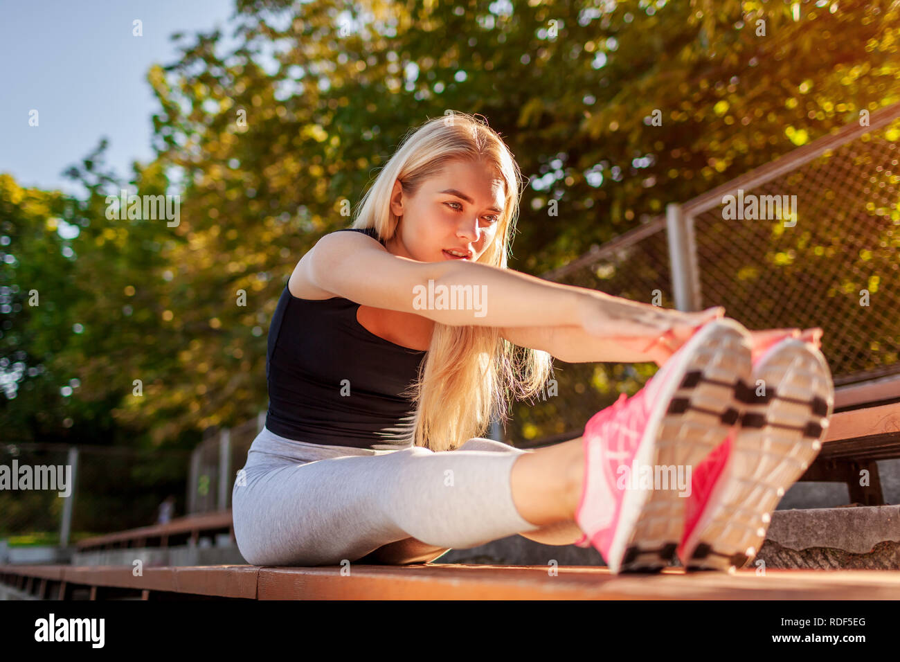 Young woman athlete warming up before running on sportsground in summer