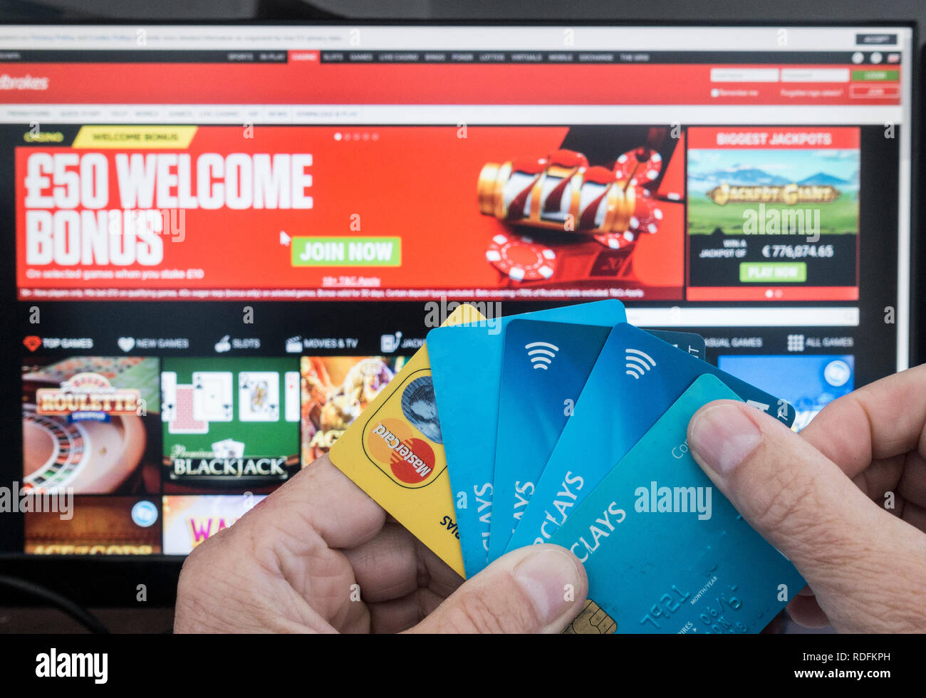 Online gambling. Person holding credit cards with Ladbrokes website on computer sreen in background. Stock Photo