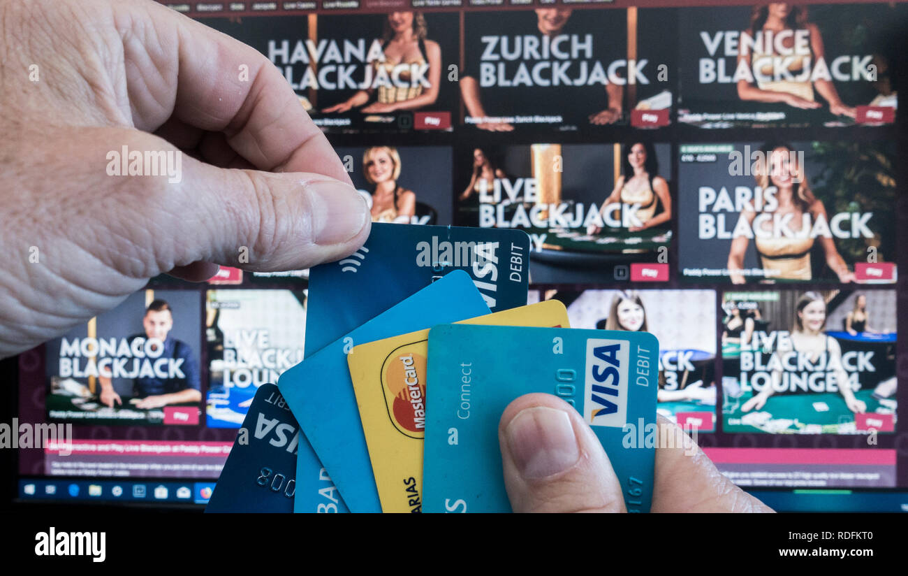 Online gambling. Person holding credit cards with Paddy Power website on computer sreen in background. Stock Photo