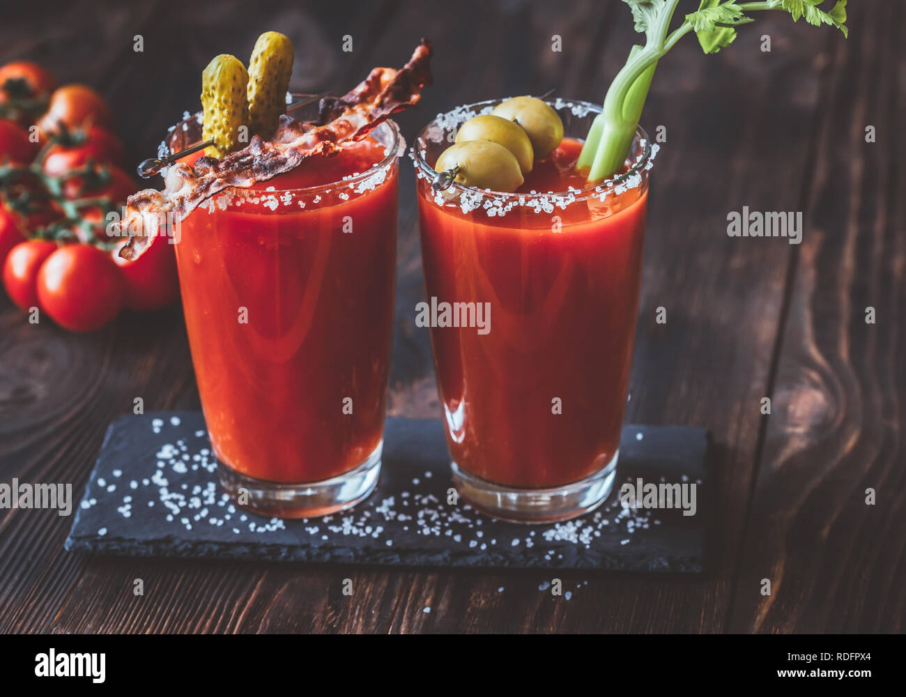 Two glasses of Bloody Mary garnished with gherkins, fried bacon strips