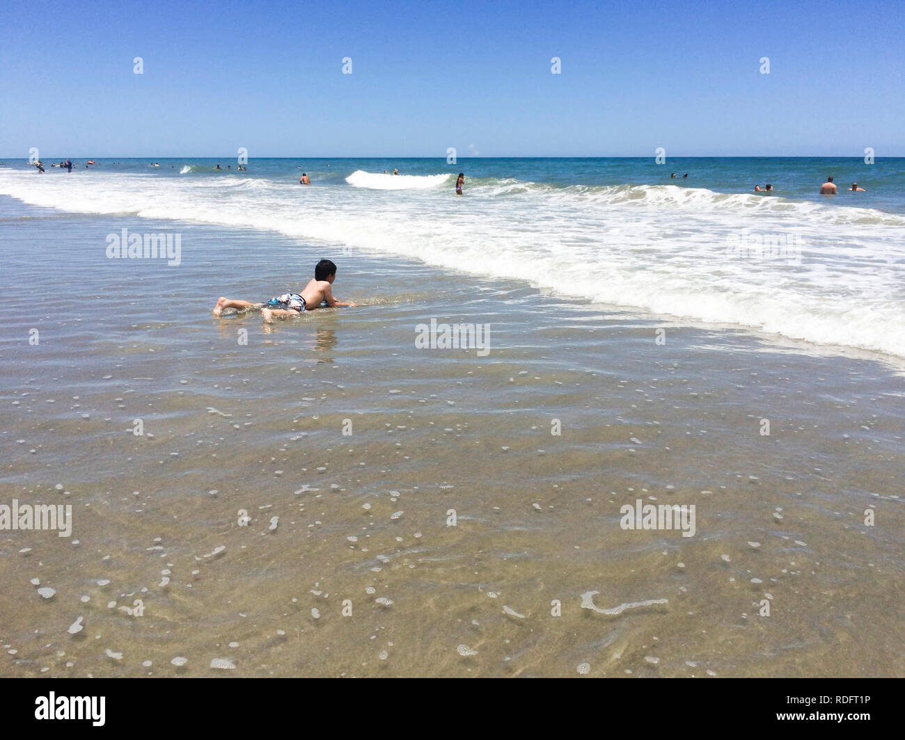 Boy playing on beach, alone (child lying in water, alone) - Cocoa Beach, Florida USA Stock Photo