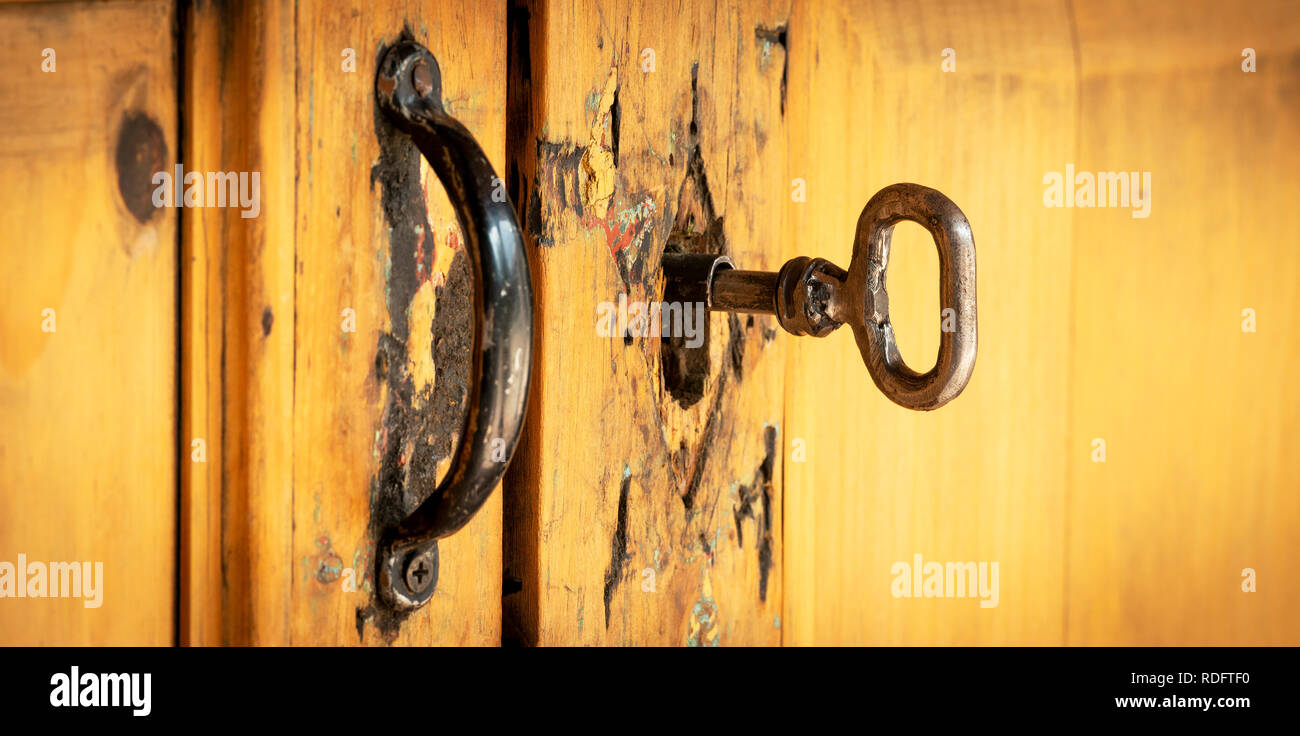 Old vintage key in a well worn wooden door lock Stock Photo