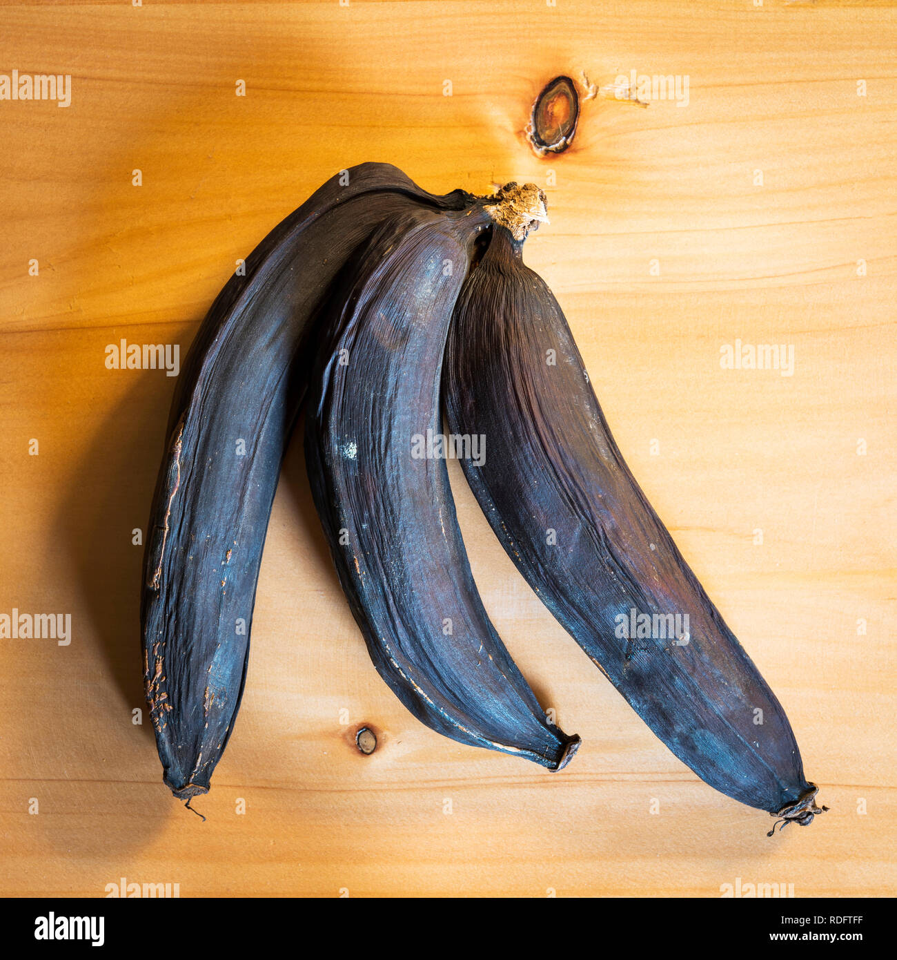 A bunch of rotten bananas that have turned black on a wooden board ...