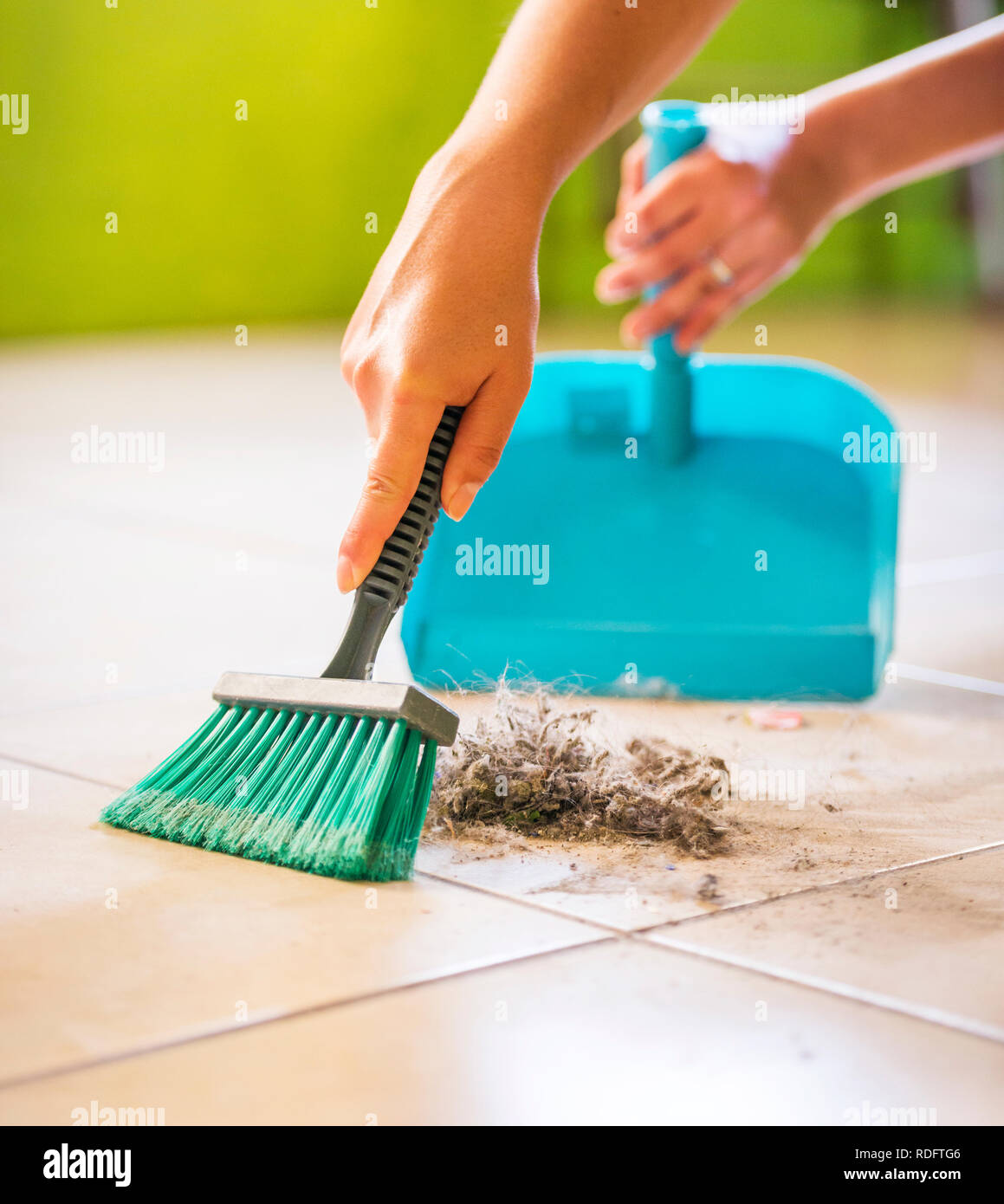 A woman sweeps up dust and dirt from the floor while cleaning the house