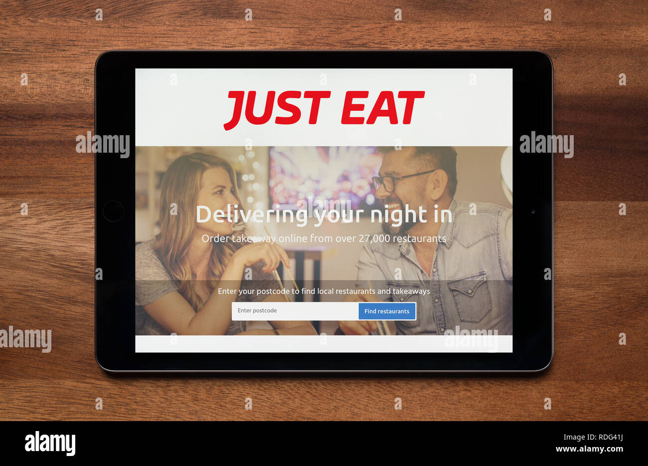 The website of Just Eat is seen on an iPad tablet, which is resting on a wooden table (Editorial use only). Stock Photo