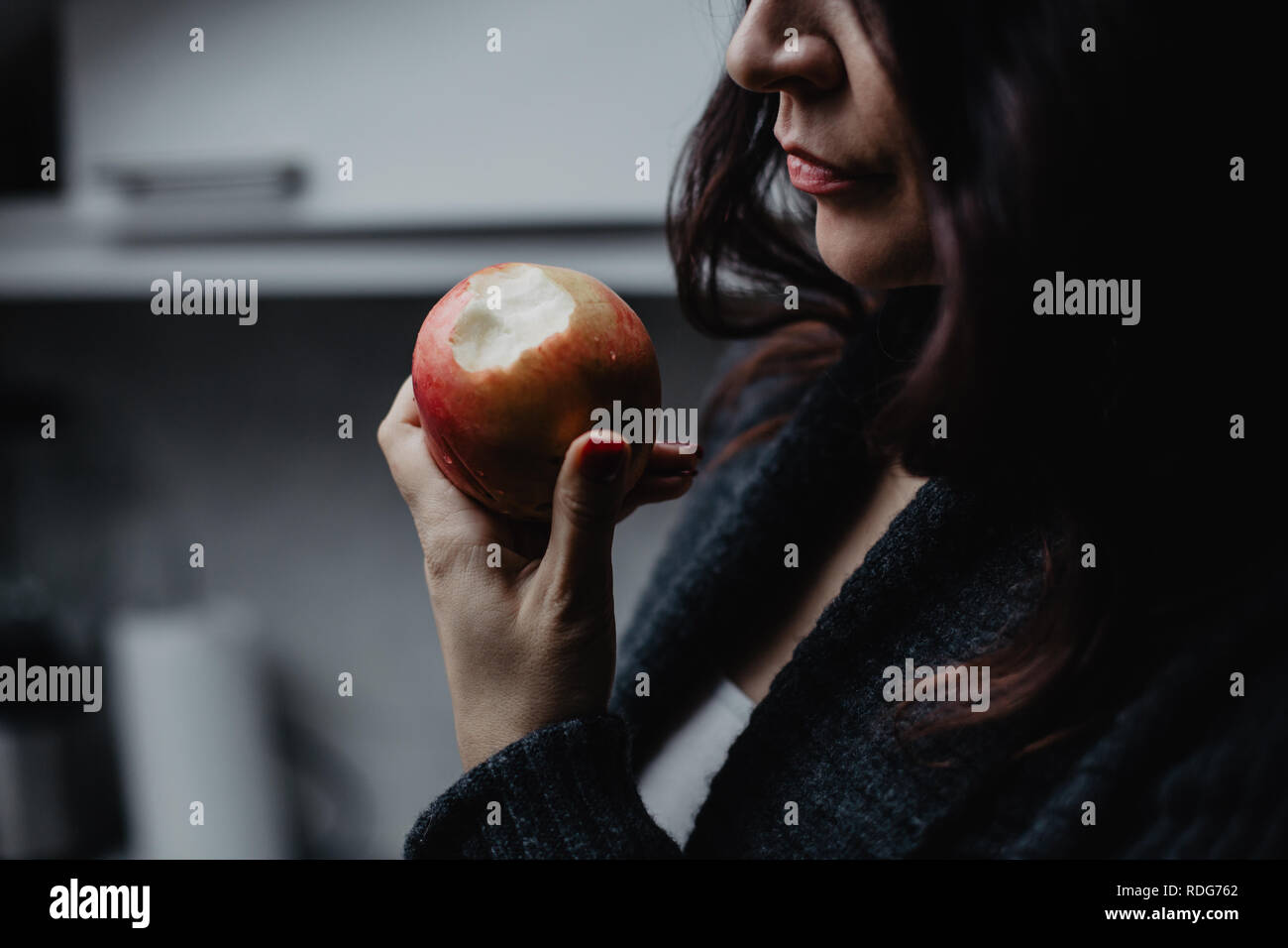 Beautiful brunette woman holding an apple in the kitchen Stock Photo