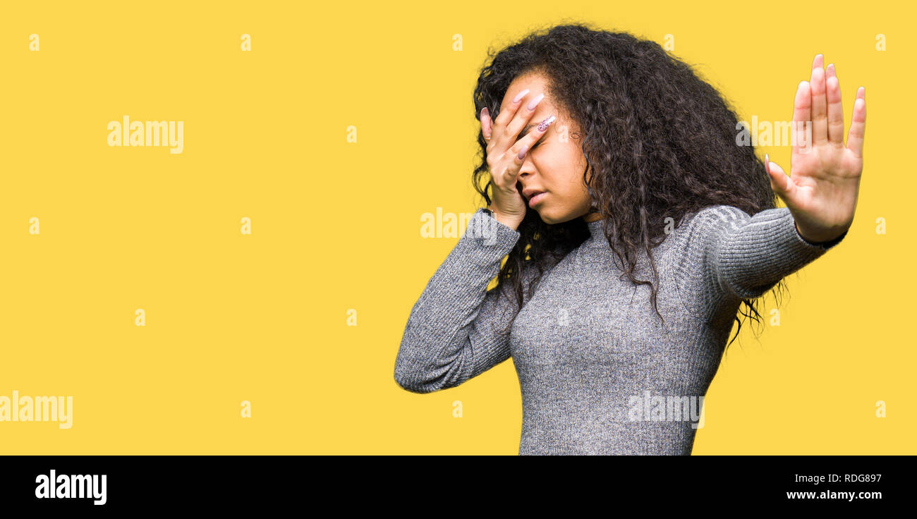 Young beautiful girl with curly hair covering eyes with hands and doing