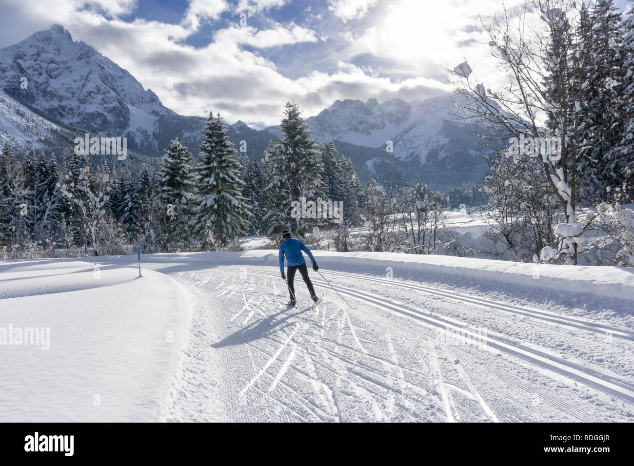 Single cross country skier on groomed ski track, sunny winter day with white clouds on blue sky. Winter mountain landscape, Ehrwald, Tirol, Austria Stock Photo