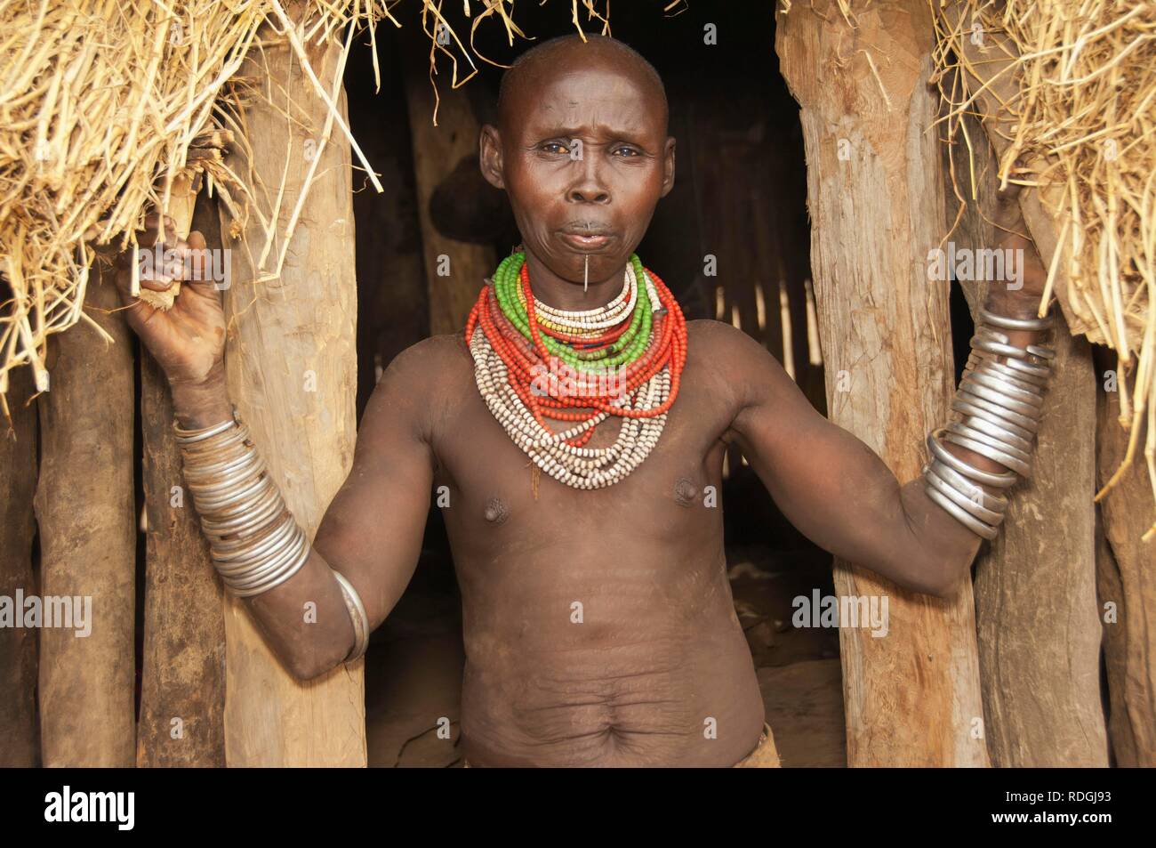 Karo woman with lots of colorful necklaces and cowry shells, lip piercing and facial paintings in front of her hut Stock Photo