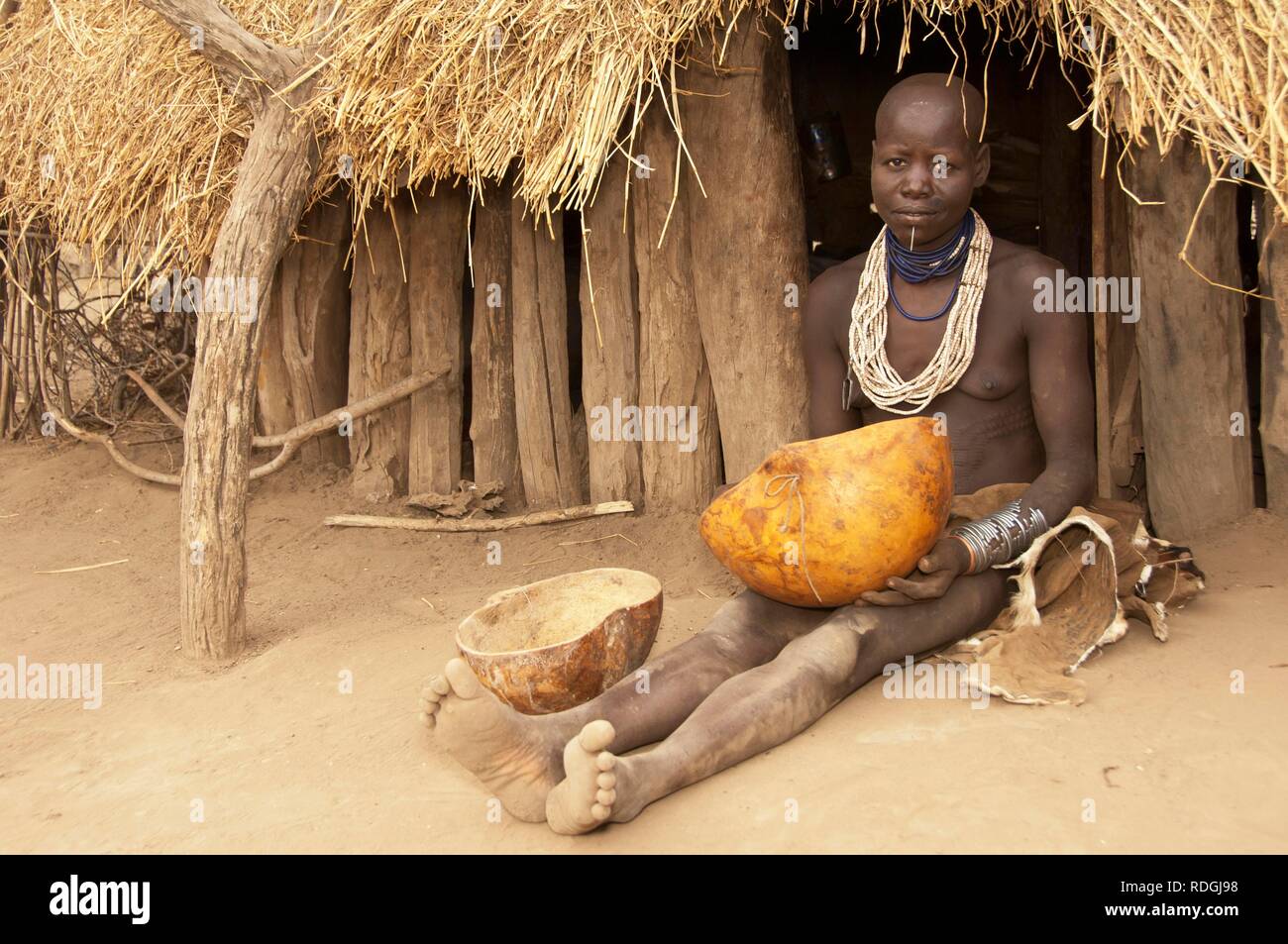 Karo woman with lots of colorful necklaces, lip piercing and calabashes in front of her hut, Omo river valley, Southern Ethiopia Stock Photo