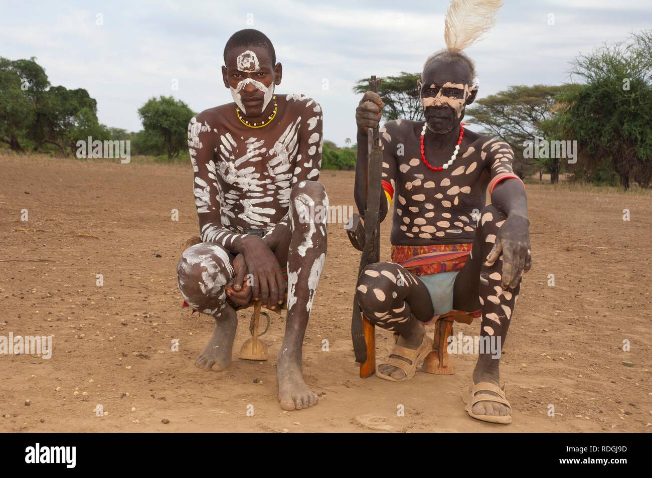 Two Karo warriors with body paintings and a rifle seated on their headrest, Omo river valley, Southern Ethiopia, Africa Stock Photo