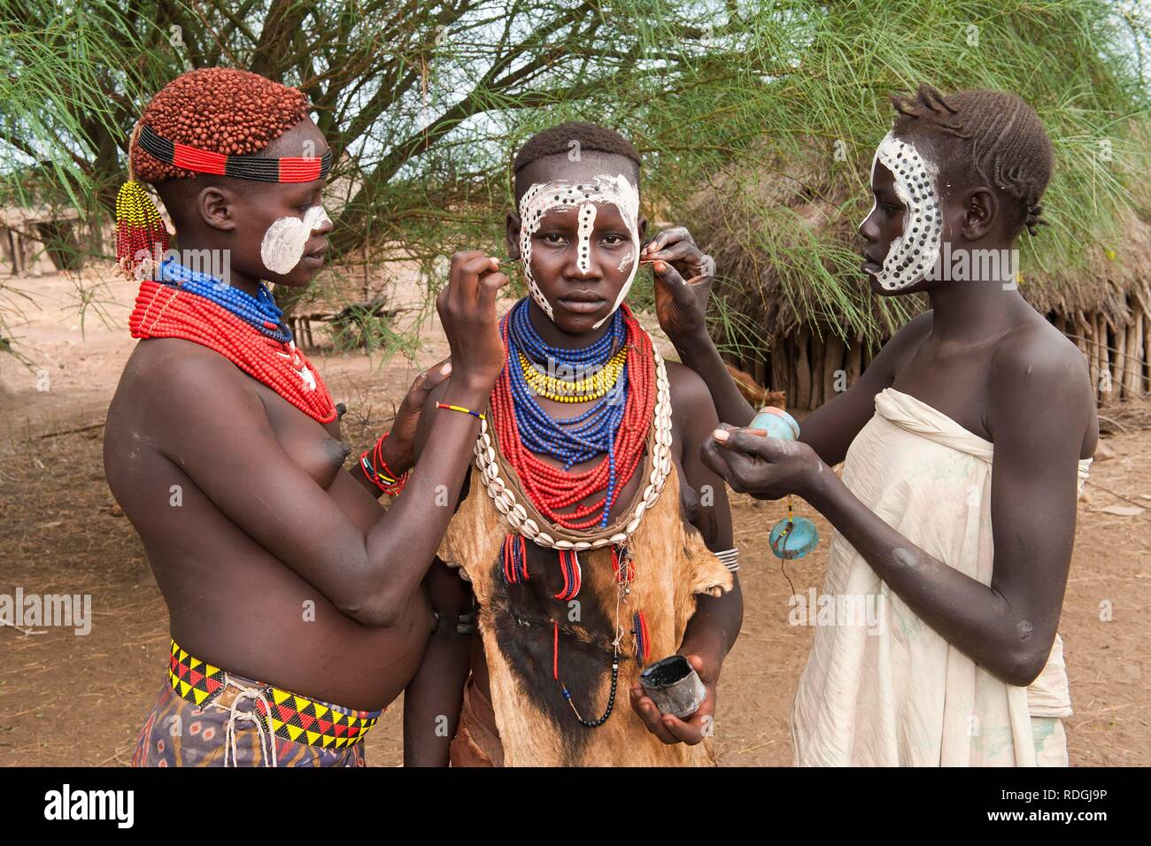 Three young Karo women putting on make-up, facial paintings, Omo river valley, Southern Ethiopia, Africa Stock Photo