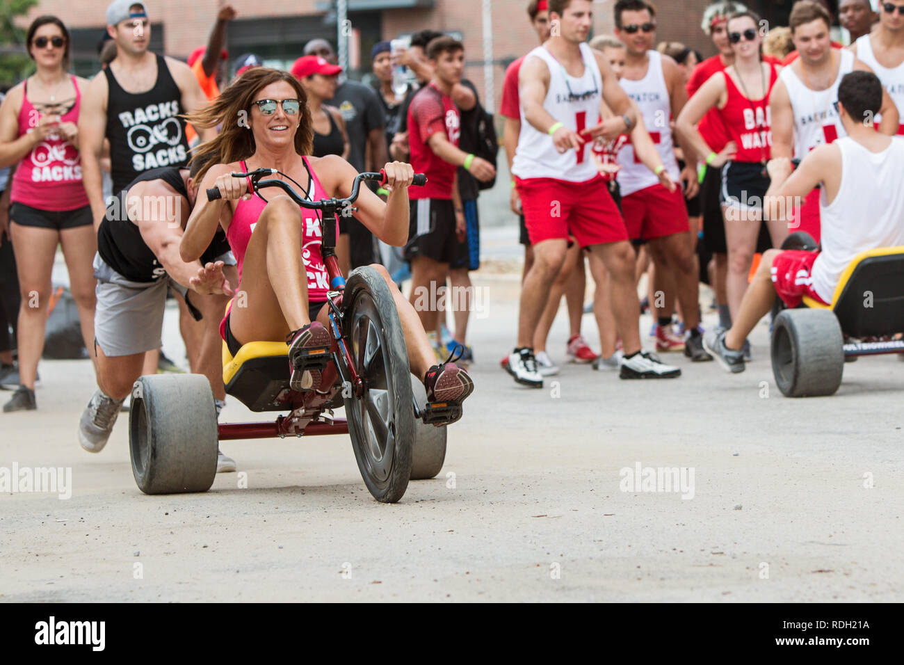 A young woman gets a push at the start line as she begins her leg of the adult big wheel relay race at Atlanta Field Day on July 14, 2018 in Atlanta. Stock Photo