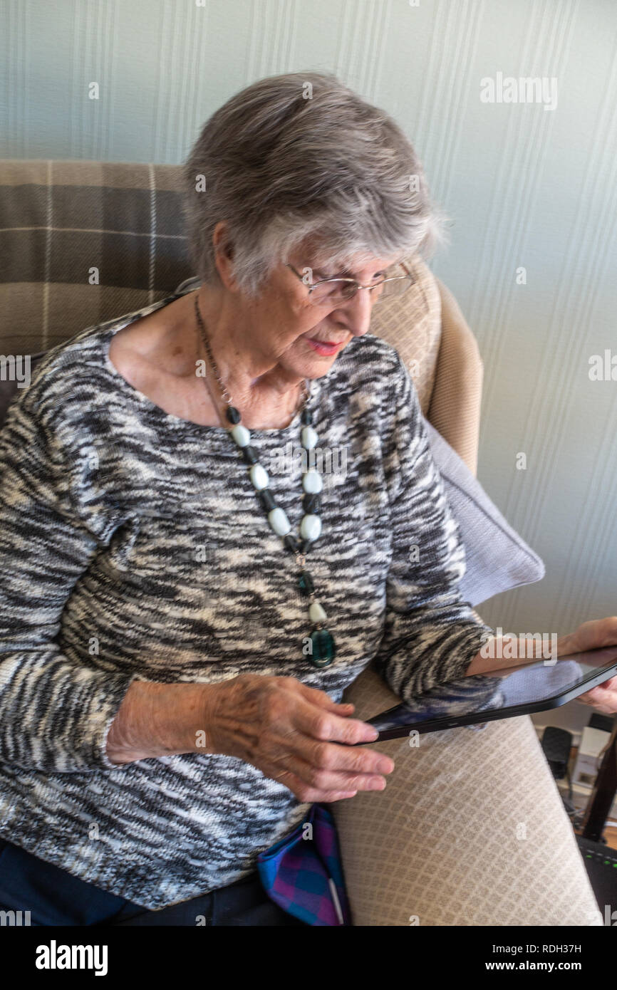 Elderly lady sitting using her personal tablet Stock Photo