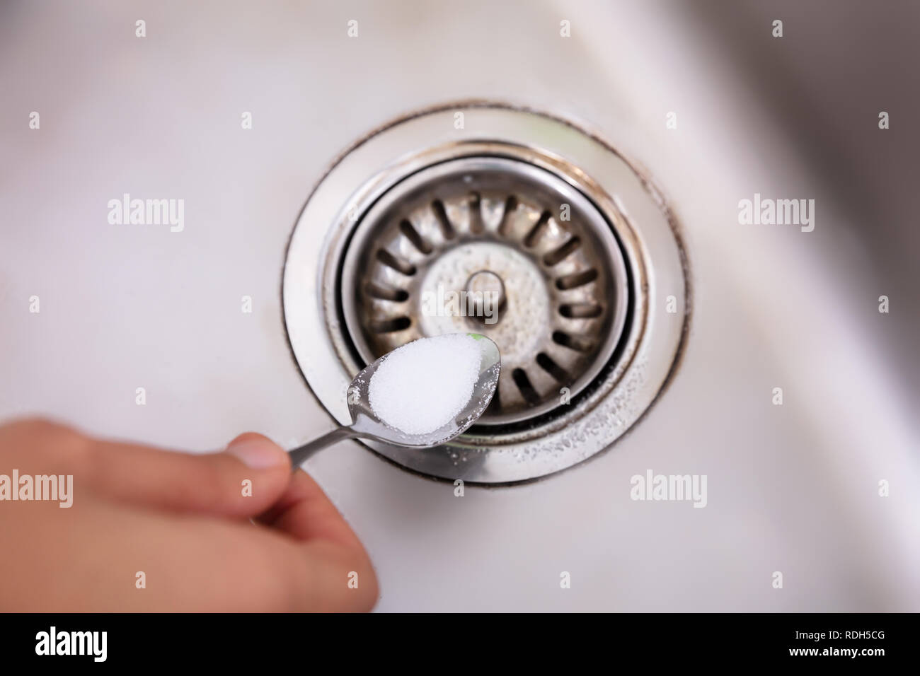 A Person Putting The Baking Soda With Spoon On Drain In The Washbasin