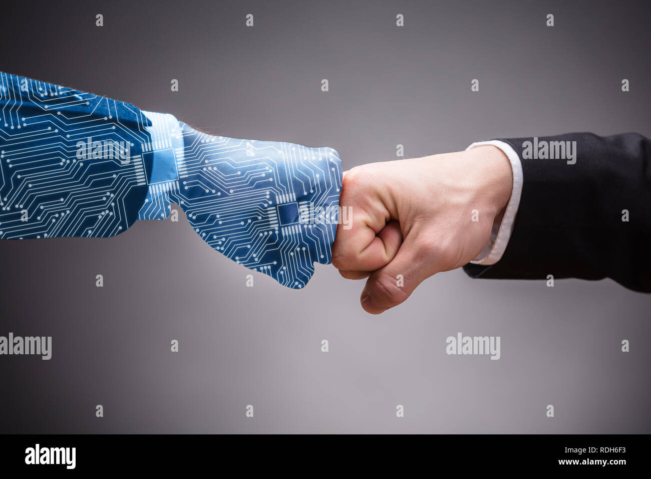 Close-up Of Digital Generated Human Hand And Businessman Making Fist Bump On Grey Background Stock Photo