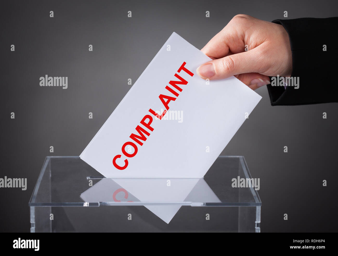 A Person's Hand Inserting Complaint Letter Into Box Slot On Grey Background Stock Photo