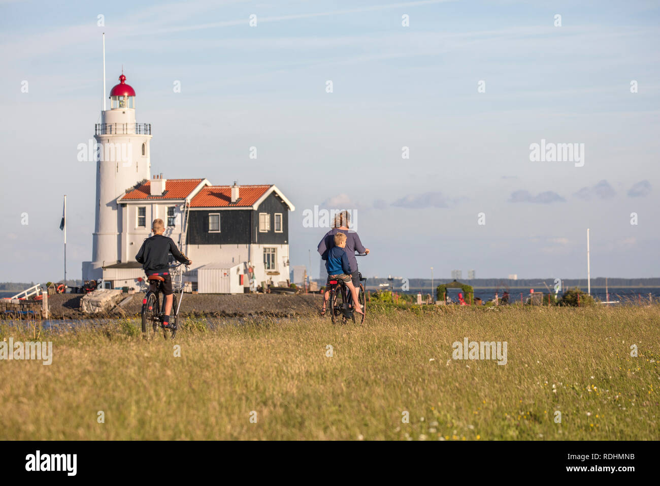 The Netherlands, Marken, Lighthouse, called Het Paard. Mother and children cycling on dyke. Stock Photo