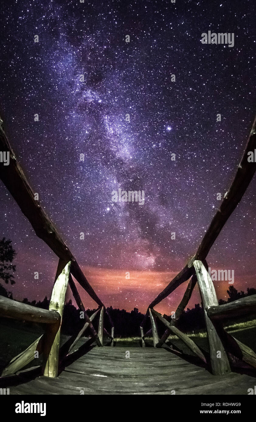 Night landscape with colorful Milky Way stars in between the wooden monkey bridge over little pond. Starry sky with bridge and trees at summer. Beauti Stock Photo