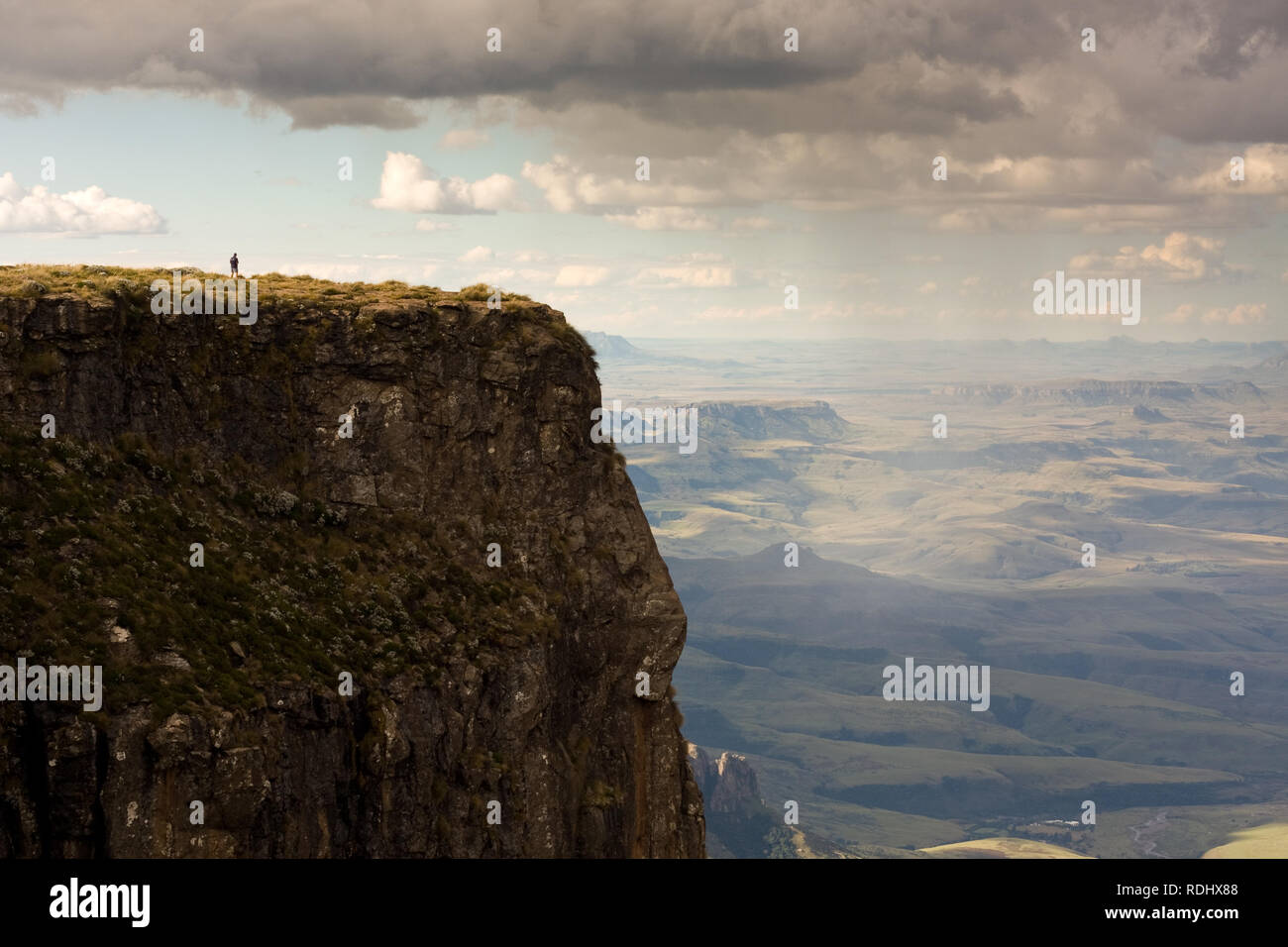 A lone hiker stands atop a scenic overlook of the Amphitheater formation in the Drakensberg, KwaZulu-Natal, South Africa. Stock Photo
