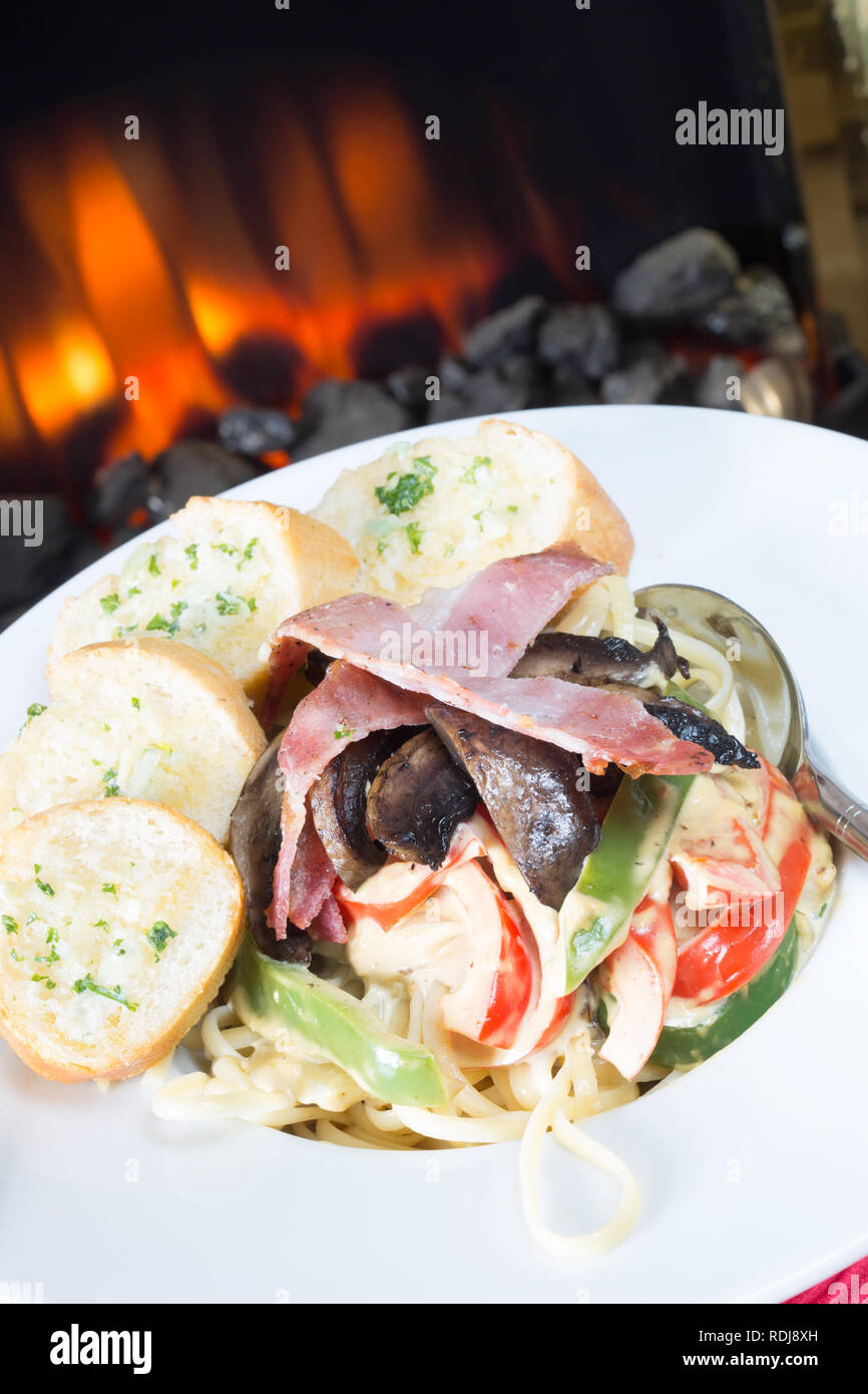 Pasta Carbonara with Linguini, mushroom and bell pepper topped with bacon and served with sliced garlic baguette Stock Photo