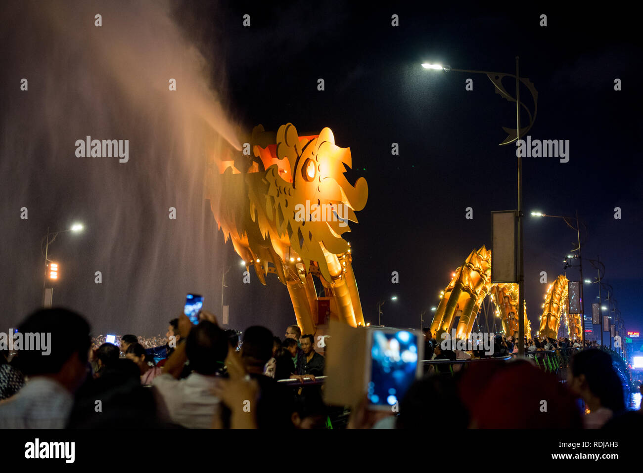 Danang, Vietnam - October 14, 2018: Danang bridge dragon spews water in the dark of night surrounded by the crowd of spectators. Stock Photo