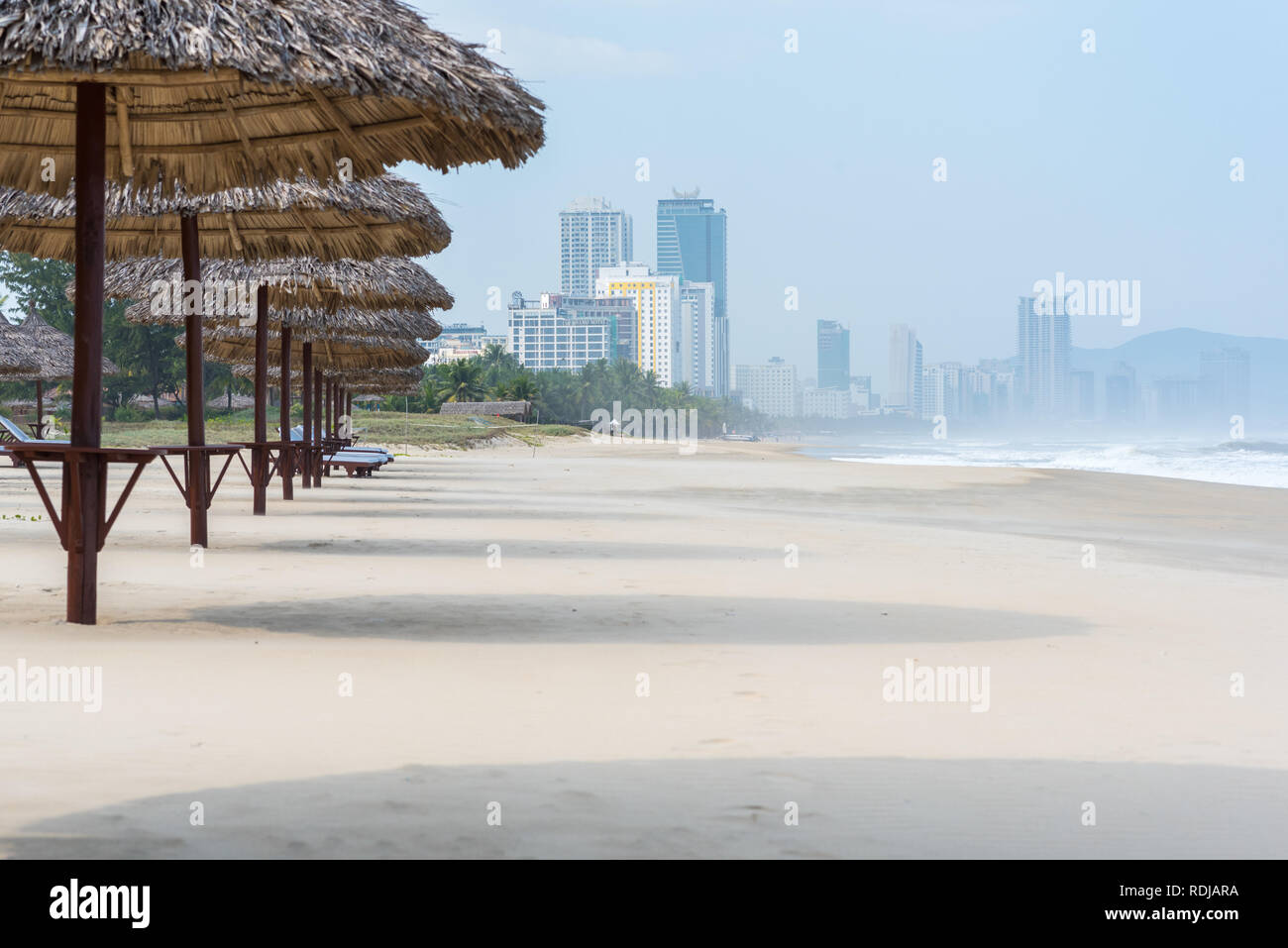 Danang, Vietnam - November 1, 2018: Thatched umbrellas along the beach with the Da Nang city skyline. Stock Photo