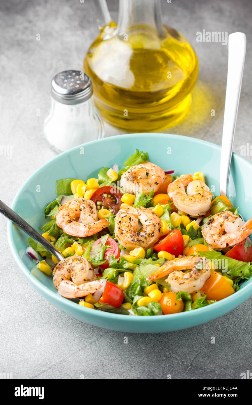 Salad with corn, fried shrimp, cherry tomatoes, red onions and lettuce in blue plate Fresh delicious lunch, healthy food Stock Photo